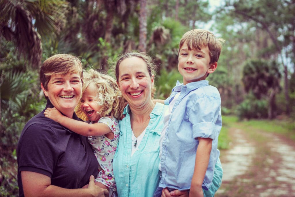 Smiling family of four posing outdoors in a green, forested park setting.
